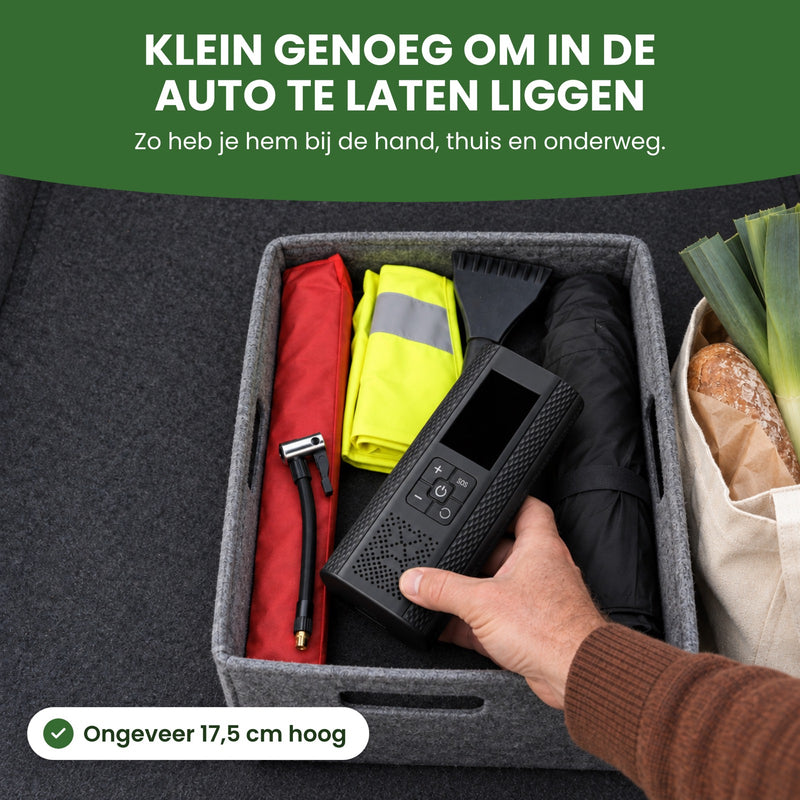 Hand legt de bandenpomp op accu in een krat in de kofferbak: klein genoeg om in de auto te laten liggen, ongeveer 17,5 cm hoog