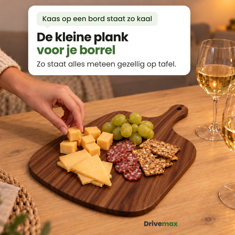 De Borrelova serveerplank op tafel met kaas, worst, crackers en druiven, naast twee glazen witte wijn; een hand pakt een blokje kaas