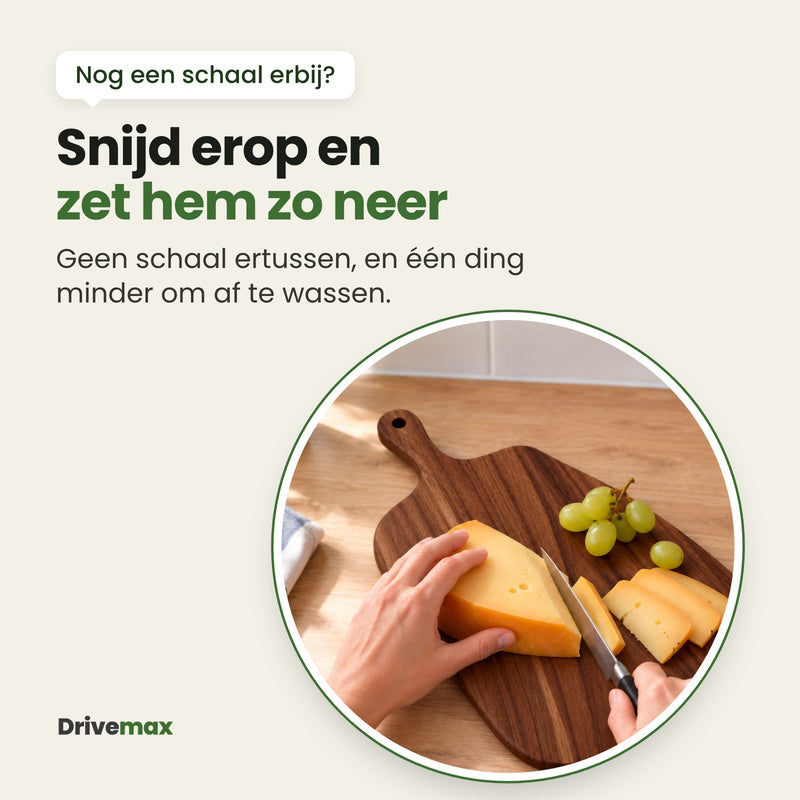 Iemand snijdt kaas op de Borrelova houten snijplank op het aanrecht, met een paar druiven op de plank