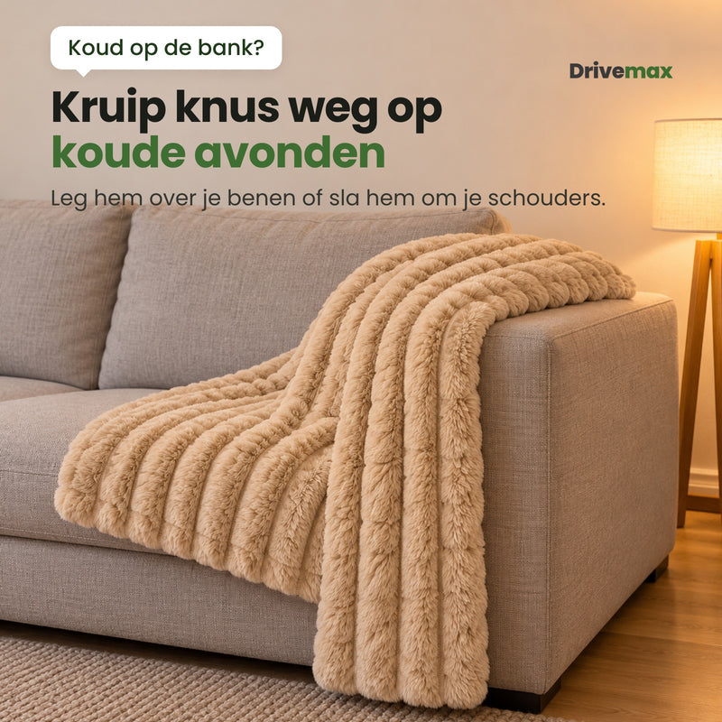 De beige Knusova plaid met ribbels over de leuning van een lichtgrijze bank in een woonkamer: kruip knus weg op koude avonden, leg hem over je benen of sla hem om je schouders
