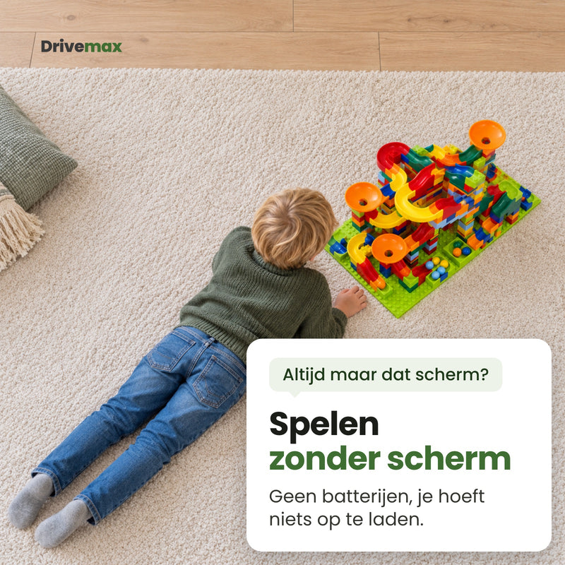 Jongen ligt op zijn buik op het kleed en kijkt naar zijn zelfgebouwde knikkerbaan: spelen zonder scherm, geen batterijen en niets op te laden