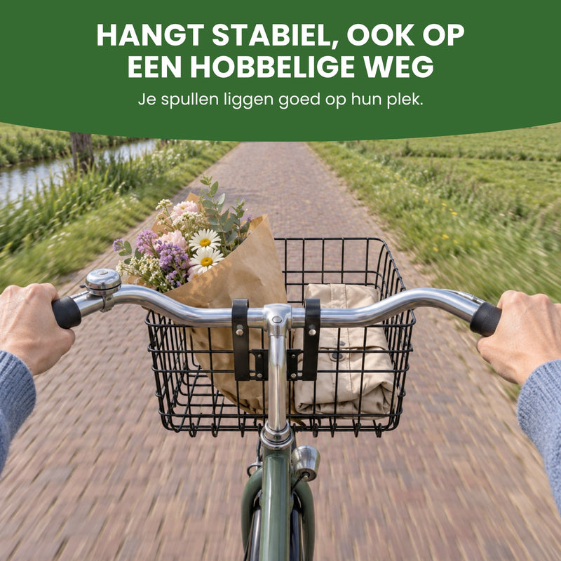 Vanaf het zadel: Trego fietsmand met bloemen en een jas, twee handen aan het stuur op een klinkerweg: hangt stabiel, ook op een hobbelige weg